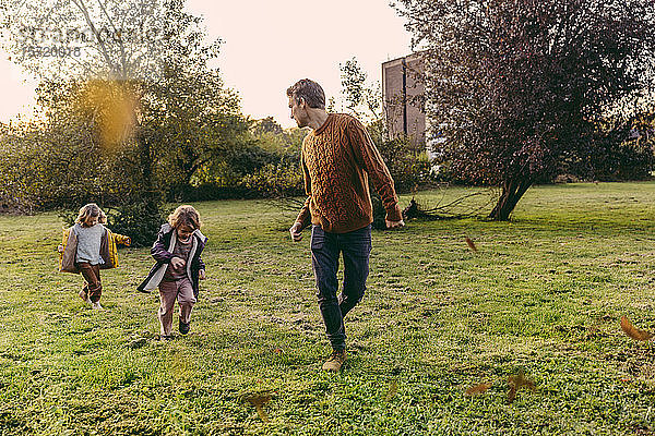 Vater läuft mit Töchtern im Herbst auf einer Wiese