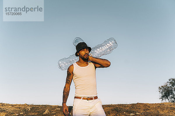 Junger Mann hält leere Plastikflaschen in unfruchtbarem Land