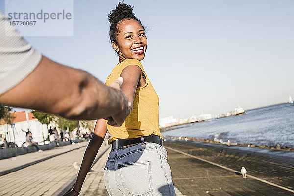 Glückliche junge Frau hält die Hand ihres Freundes am Pier am Wasser  Lissabon  Portugal