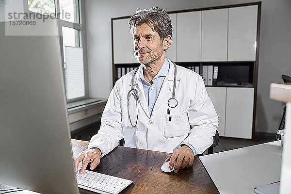 Arzt mit Computer am Schreibtisch in seiner Praxis