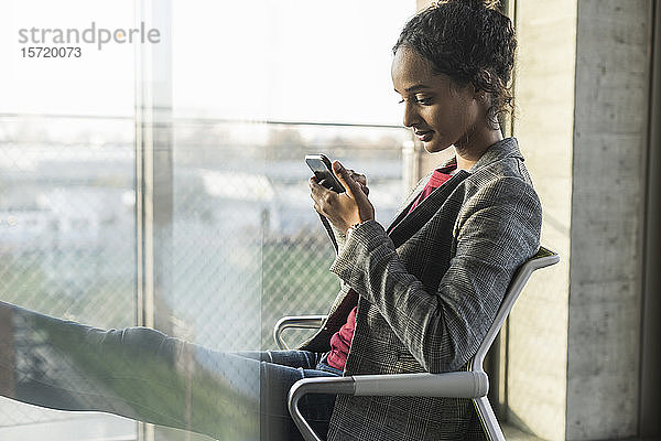 Junge Geschäftsfrau benutzt Handy am Fenster im Büro