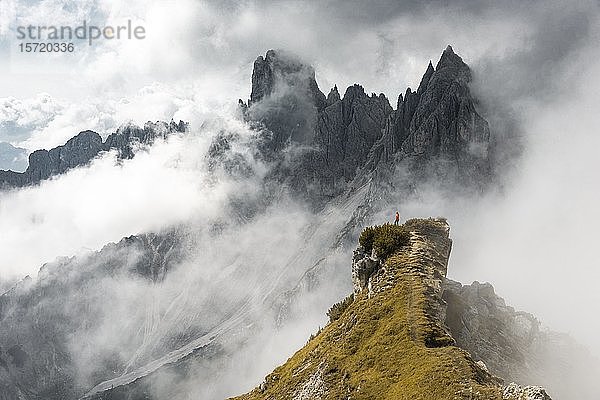 Frau in roter Jacke auf einem Bergrücken stehend  hinter Bergspitzen und spitzen Felsen  dramatische Wolken  Cimon di Croda Liscia und Cadini-Gruppe  Auronzo di Cadore  Belluno  Italien  Europa