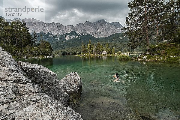 Frau schwimmt im See  Blick auf Eibsee vor Zugspitzmassiv mit Zugspitze  bewölkt  Wettersteingebirge  bei Grainau  Oberbayern  Bayern  Deutschland  Europa