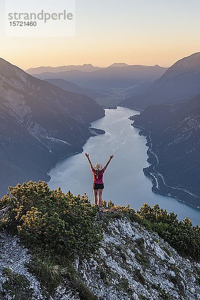 Sonnenuntergang  junge Frau blickt über Berglandschaft und streckt die Arme in die Luft  Blick vom Bärenkopf zum Achensee  Tirol  Österreich  Europa