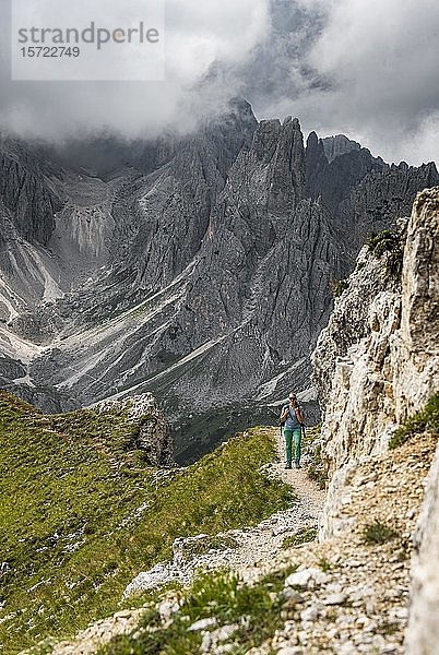 Junge Frau  Bergsteigerin auf einem Wanderweg  hinter Bergspitzen und scharfen Felsgipfeln  bewölkter Himmel  Cimon di Croda Liscia und Cadini-Gruppe  Sextner Dolomiten  Belluno  Italien  Europa