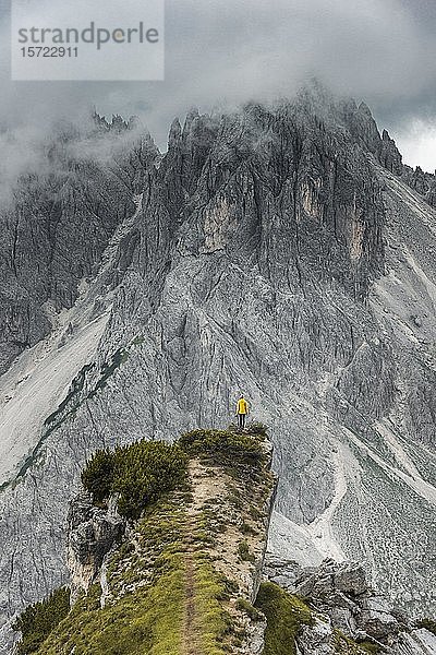 Frau in gelber Jacke auf einem Bergrücken stehend  hinter ihr Bergspitzen und scharfe Felsgipfel  bewölkter Himmel  Cimon die Croda Liscia und Cadini Gruppe  Auronzo di Cadore  Belluno  Italien  Europa