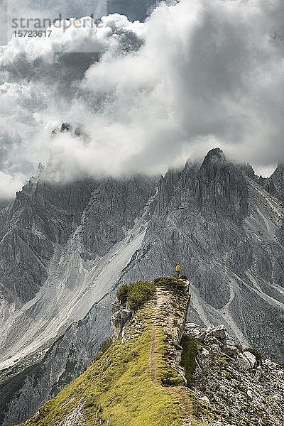 Frau in gelber Jacke steht auf einem Bergrücken  hinter ihr Felswand  dramatische Wolken  Cimon die Croda Liscia und Cadini Gruppe  Auronzo di Cadore  Belluno  Italien  Europa