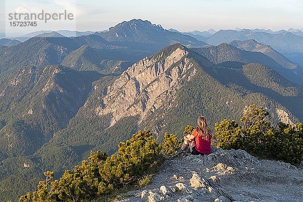 Junge Frau sitzt auf dem Gipfel  Blick vom Herzogstand  Jochberg und Alpen  Oberbayern  Bayern  Deutschland  Europa