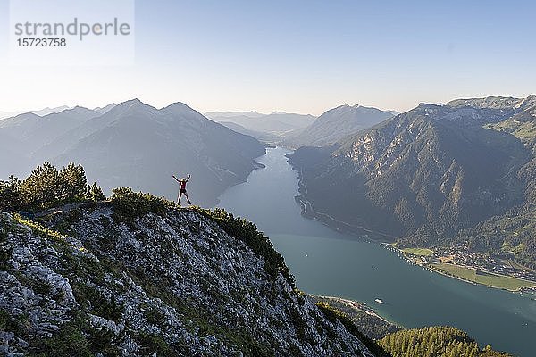 Junge Frau springt in die Luft  Blick vom Bärenkopf zum Achensee  links Seebergspitze und Seekarspitze  rechts Rofangebirge  Tirol  Österreich  Europa