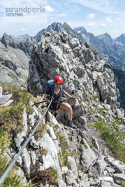 Lachende junge Frau mit Kletterhelm am gesicherten Felsen  Kletterin auf einem Klettersteig  Mittenwalder Klettersteig  Karwendelgebirge  Mittenwald  Deutschland  Europa