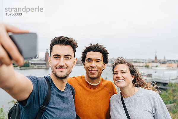 Lächelnde Freunde beim Selfie mit dem Handy  während sie in der Stadt gegen den Himmel stehen