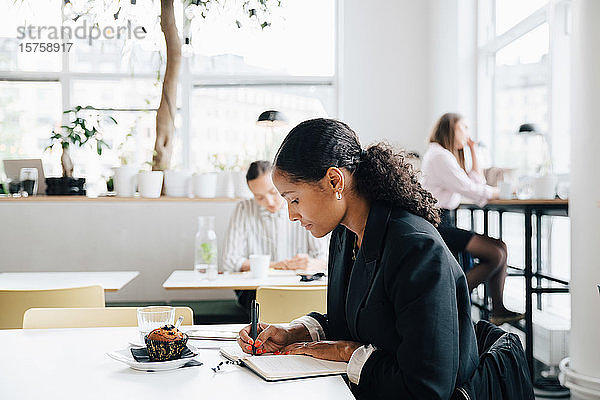 Geschäftsfrau schreibt Tagebuch  während sie einen Muffin in der Büro-Cafeteria isst