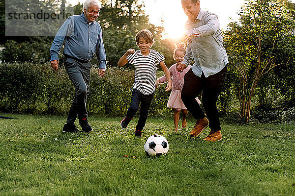 Fußball spielende Mehrgenerationen-Familie in voller Länge im Hinterhof