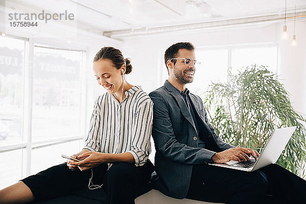 Lächelnde Geschäftskollegen mit Smartphone und Laptop im Kreativbüro
