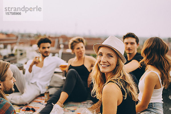 Porträt einer lächelnden Frau  die während einer Dachfeier mit Freunden auf der Terrasse sitzt
