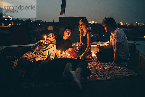 Freunde genießen Wein bei Kerzenlicht  während sie in der Abenddämmerung auf einer Terrasse in der Stadt entspannen