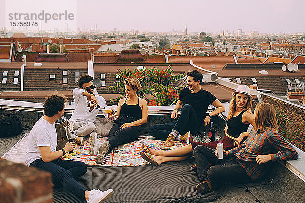 Fröhliche Freunde genießen Bier auf der Terrasse während einer Dachfeier in der Stadt