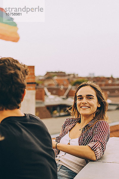 Porträt einer glücklichen Frau  die mit einem Freund auf einer Terrasse gegen den Himmel sitzt