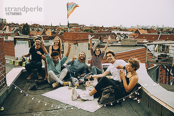 Glückliche männliche und weibliche Freunde jubeln auf der Terrasse  während sie sich auf der Dachparty in der Stadt amüsieren