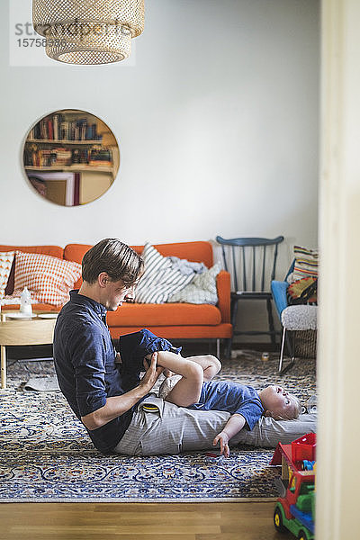 Seitenansicht eines Mannes  der einem Kleinkind beim Anziehen im heimischen Wohnzimmer hilft