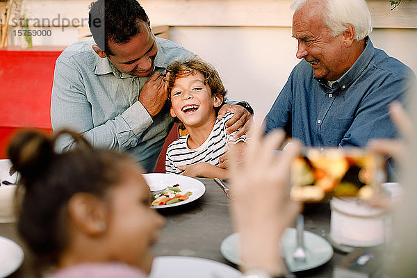 Ältere Frau fotografiert glückliche Familie am Esstisch während des Mittagessens