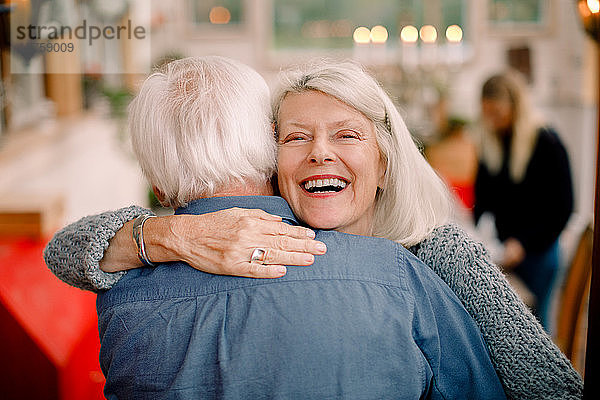 Porträt einer älteren Frau  die einen Mann umarmt  während sie zu Hause steht
