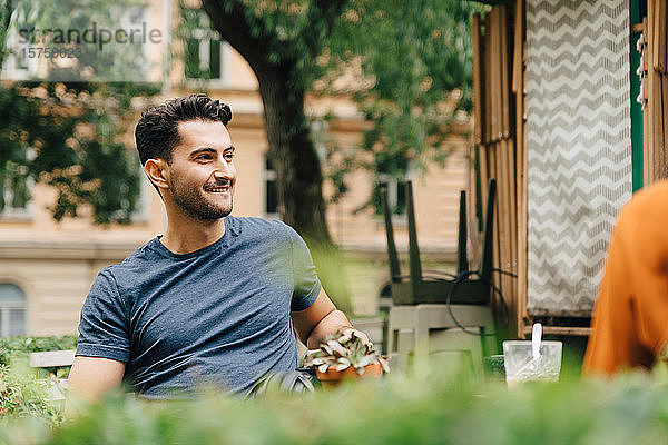 Lächelnder junger Mann sitzt mit Freund im Restaurant in der Stadt