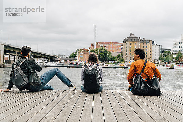 Rückansicht von Freunden  die auf dem Pier am Fluss in der Stadt gegen den Himmel sitzen