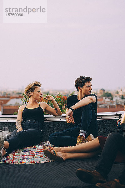 Freundinnen und Freunde schauen weg  während sie auf einer Terrasse in der Stadt zusammensitzen