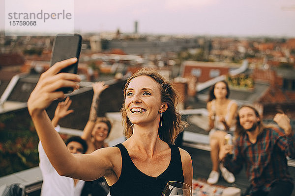 Lächelnde junge Frau  die mit Freunden per Smartphone auf der Terrasse Selbsthilfe betreibt