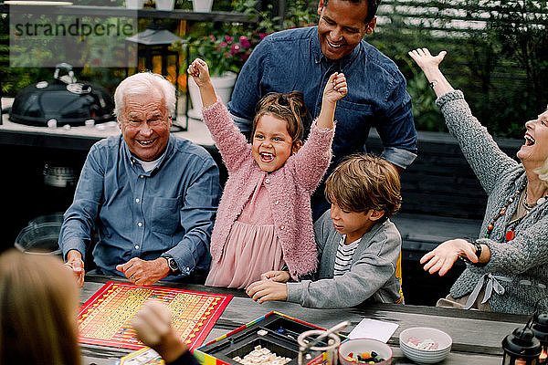 Fröhliche Mehrgenerationen-Familie spielt Brettspiel am Tisch  während sie auf der Terrasse sitzt