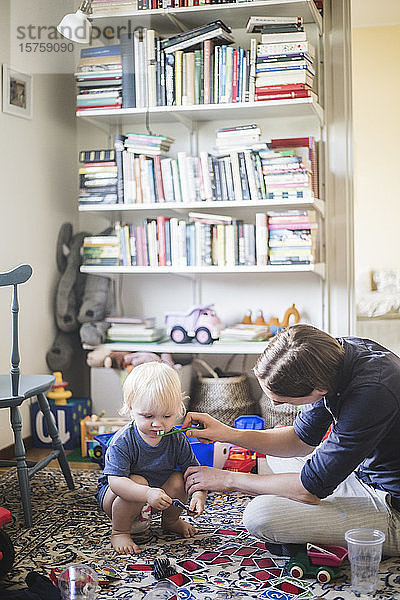 Mann putzt Kleinkindern beim Spielen zu Hause im Wohnzimmer die Zähne