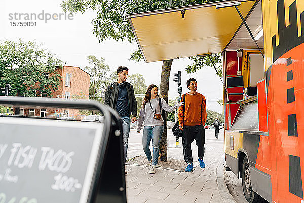 Freunde in voller Länge zu Fuß auf der Straße mit einem Speisewagen in der Stadt