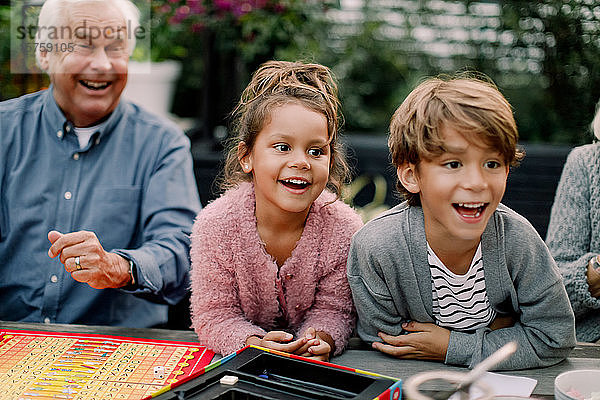 Lächelnde Enkel spielen Brettspiel mit den Großeltern auf dem Tisch im Hinterhof