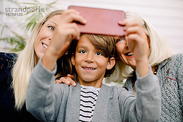 Lächelnder Junge nimmt sich mit Mutter und Großmutter im Handy mit
