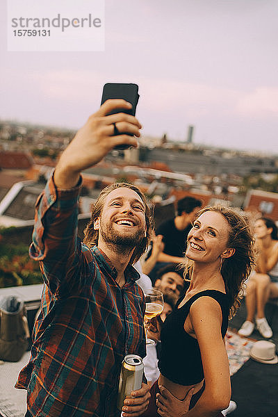 Glücklicher Mann nimmt sich mit fröhlichen Freunden während einer Dachparty auf der Terrasse
