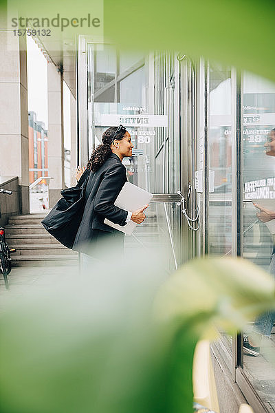 Lächelnde Geschäftsfrau öffnet Tür und betritt Büro