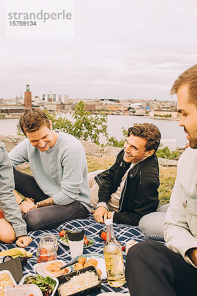 Glückliche männliche Freunde genießen das Essen beim Picknick gegen den Himmel