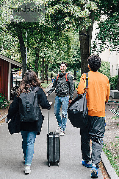 Freunde in voller Länge mit Gepäck auf der Straße bei Bäumen in der Stadt