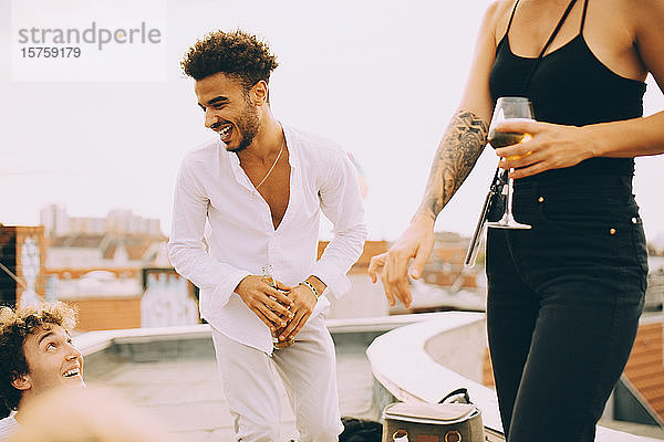 Fröhlicher junger Mann tanzt und trinkt bei einer Party mit Freunden auf der Terrasse