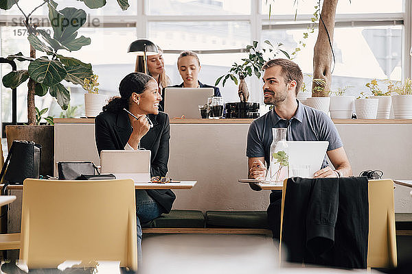 Männliche und weibliche Kollegen diskutieren während der Arbeit am Schreibtisch im Coworking Space