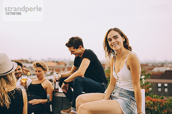 Lächelnde junge Frau sitzt mit Freunden auf einer Dachfeier