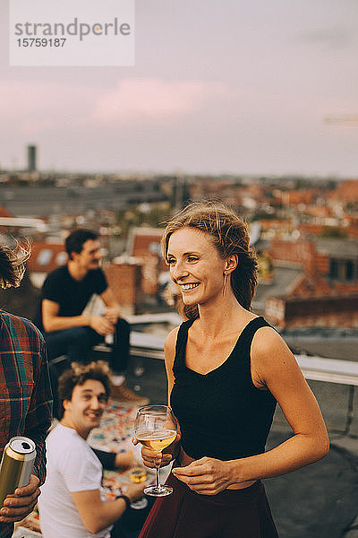 Lächelnde junge Frau genießt Bier mit Freunden auf einer Dachparty
