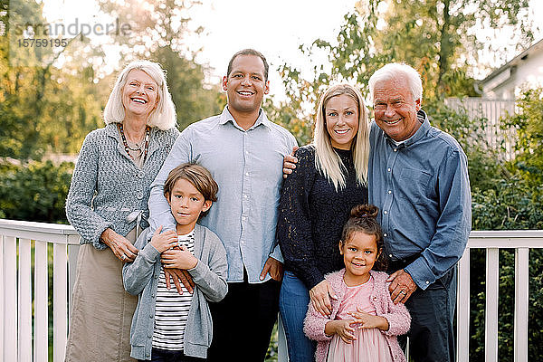 Porträt einer lächelnden Mehrgenerationen-Familie  die im Hinterhof vor einem Geländer steht
