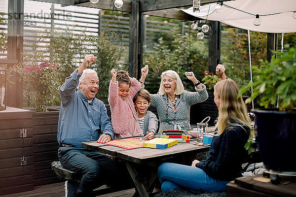 Fröhliche Familie spielt Brettspiel  während sie im Hinterhof am Tisch sitzt