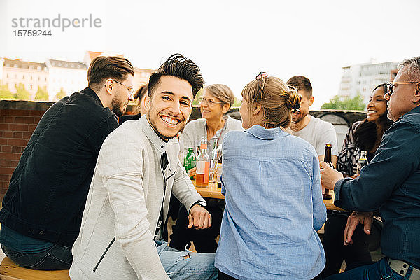 Porträt eines glücklichen Mannes  der mit Freunden zusammensitzt und sich in geselliger Runde amüsiert