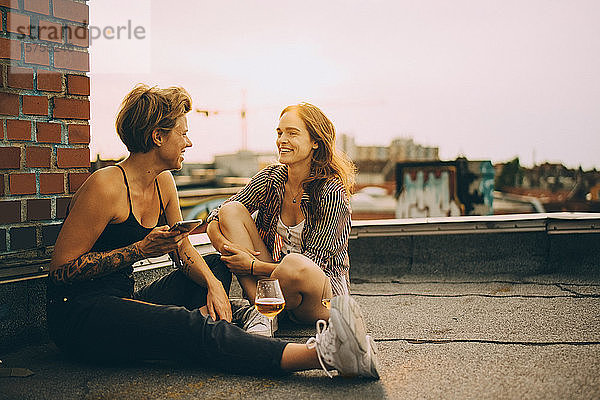 Fröhliche Freundinnen unterhalten sich während einer Dachparty auf einer Terrasse in der Stadt