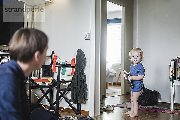 Säugling in voller Länge hält digitales Tablett in der Hand  während er den Vater im Wohnzimmer anschaut