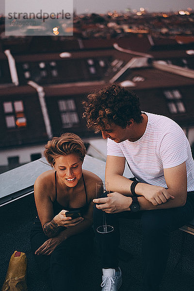 Hochwinkelansicht eines Mannes  der Wein trinkt  während er einen Freund mit seinem Handy auf der Terrasse anschaut
