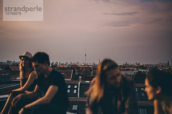 Freunde unterhalten sich auf der Terrasse während einer Dachfeier in der Stadt in der Abenddämmerung